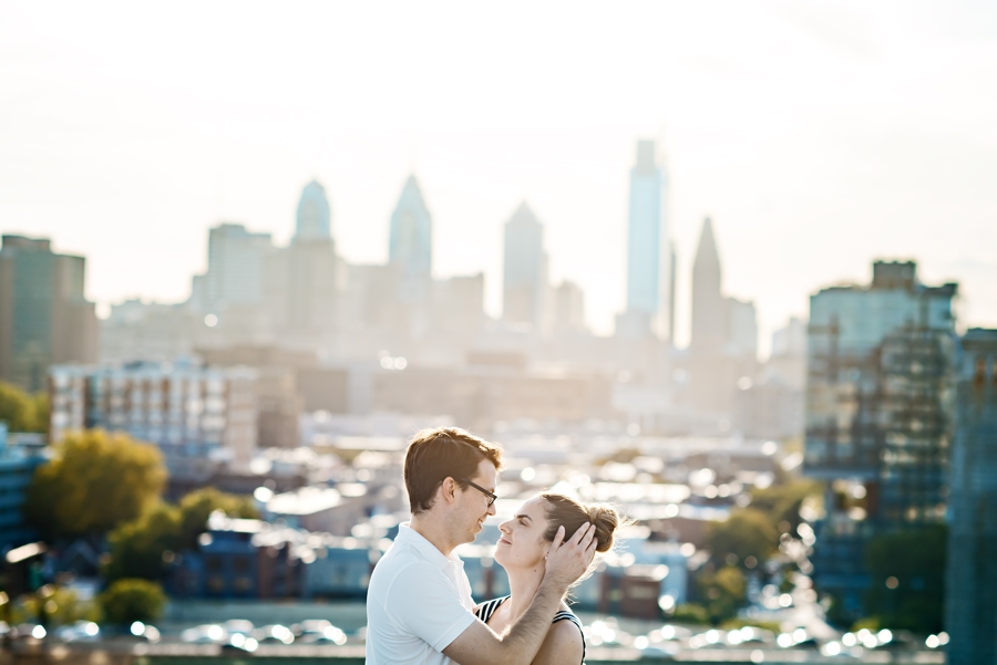 An engaged couple kiss on the ben franklin bridge with the Philadelphia skyline in the background.